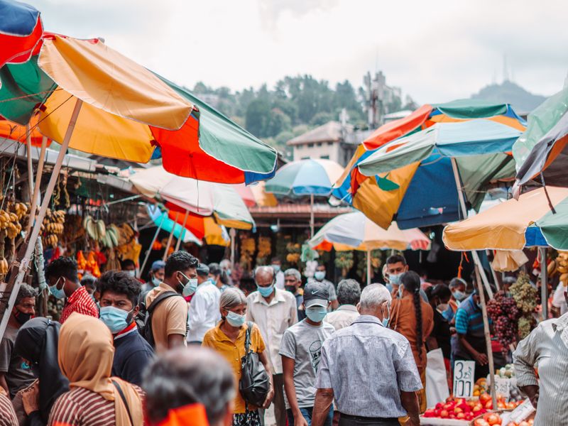 A busy outdoor Sri Lankan fair with colourful umbrellas shading the stalls.