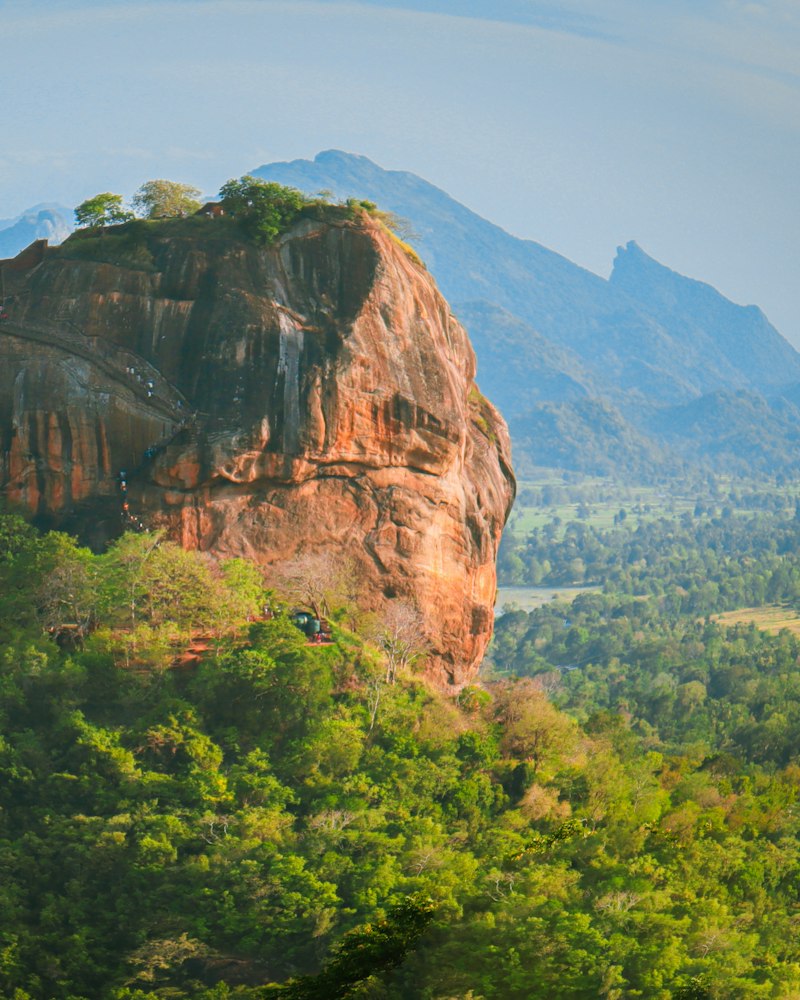 Sigiriya Rock fortress seen across still water and palm trees